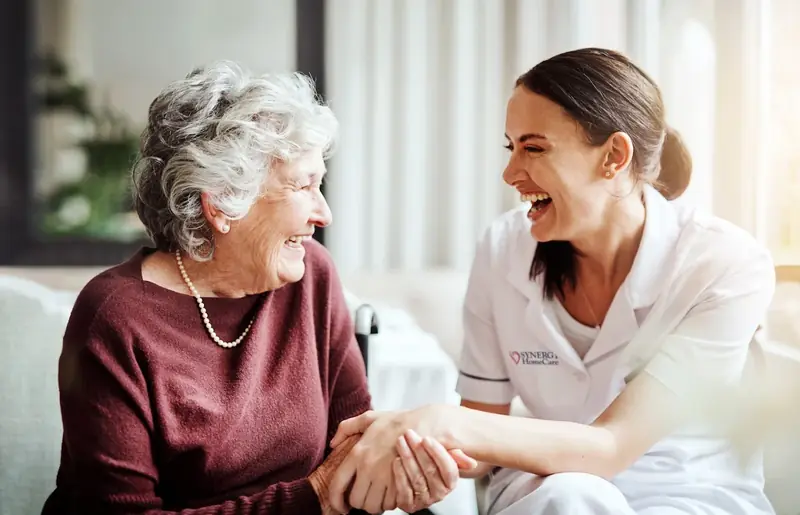 An older woman and her caregiver sitting together at home, relaxed and at ease